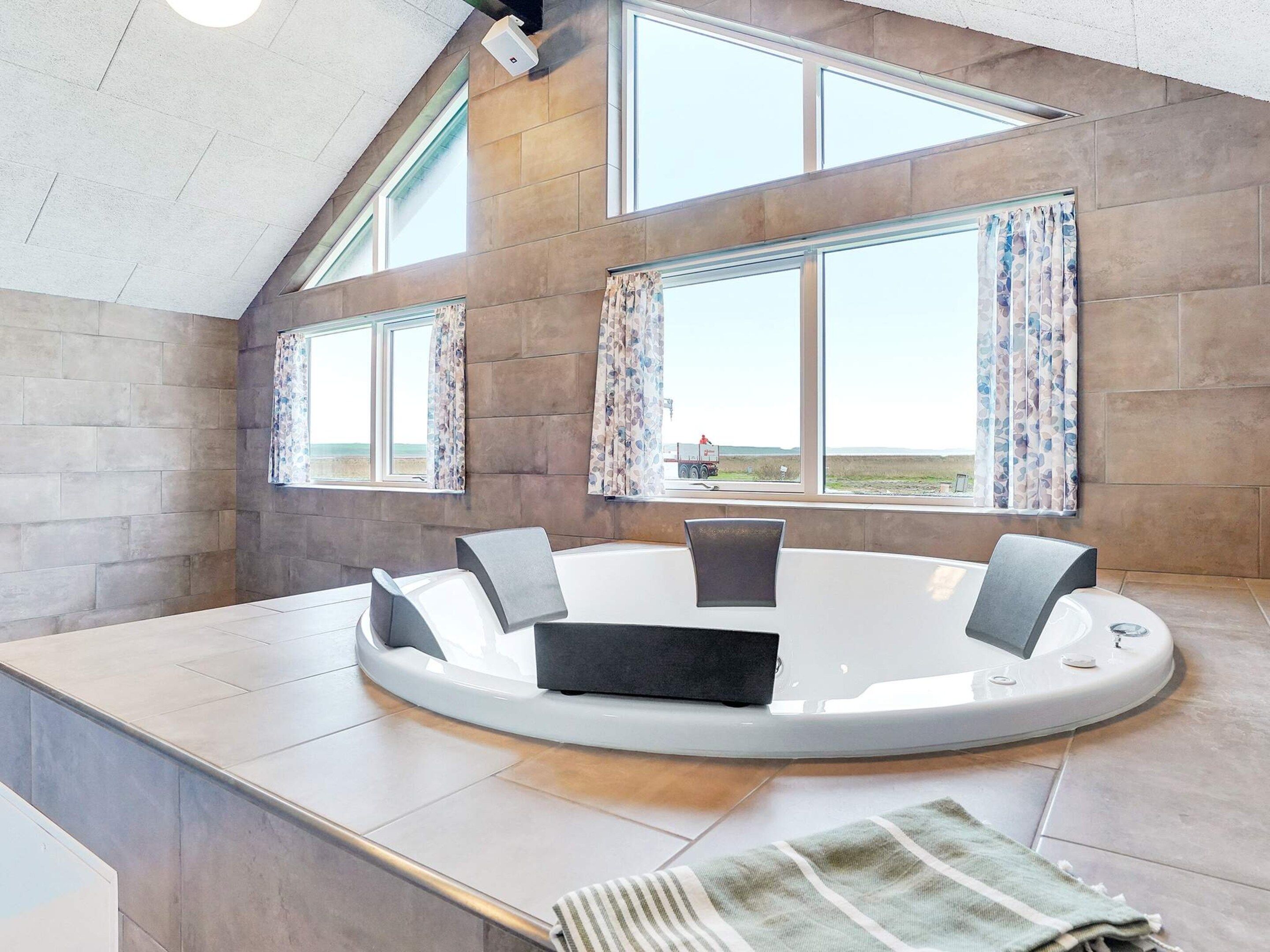 A modern bathroom with a circular bathtub, large windows, and a view of the landscape.