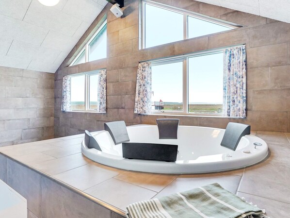 A modern bathroom with a circular bathtub, large windows, and a view of the landscape.