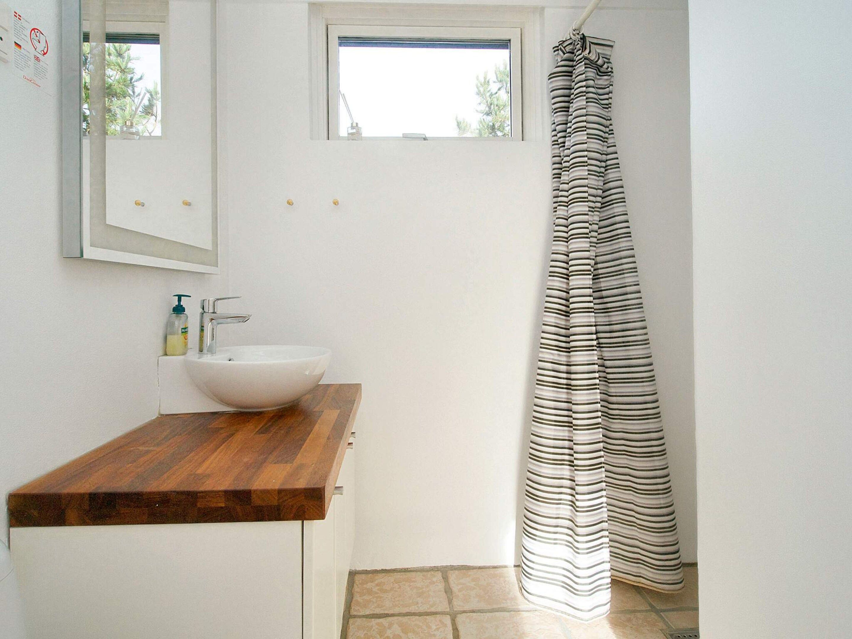Une salle de bain avec un plan de toilette en bois, un lavabo blanc, un rideau de douche à rayures et une petite fenêtre au-dessus du lavabo.