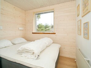 A room with wooden walls, a bed with white bedding, a window with a view of trees, and a wall with framed pictures. - 4 Person Holiday Home in Holbaek (Holbaek)