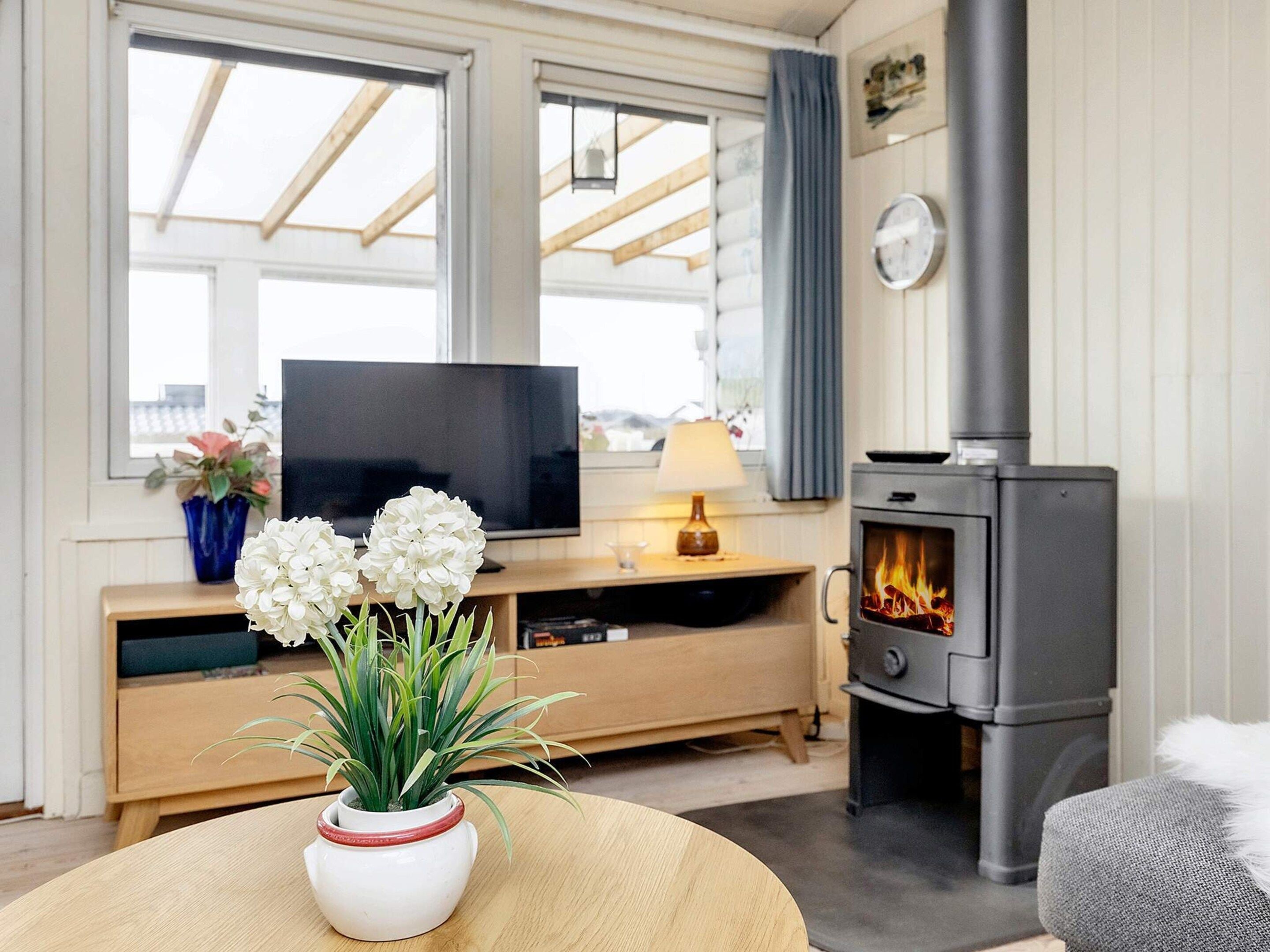 Ein gemütliches Wohnzimmer mit Fernseher, Kamin und einem runden Tisch mit Blumen in einer Vase.