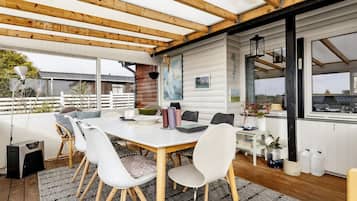 A covered outdoor dining area with a table, chairs, and a view of the surrounding landscape.