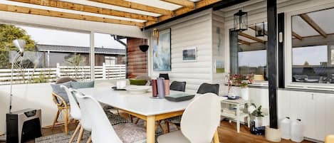 A covered outdoor dining area with a table, chairs, and a view of the surrounding landscape.