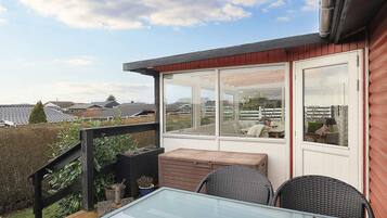 A glass-top table with wicker chairs on a wooden deck, overlooking a residential area.