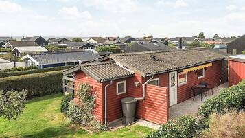 A red wooden house with a tiled roof, surrounded by a well-maintained lawn and hedges.