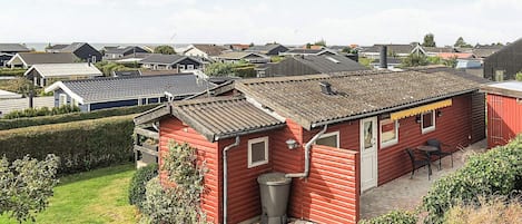 A red wooden house with a tiled roof, surrounded by a well-maintained lawn and hedges.
