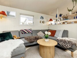 Una sala de estar acogedora con un sofá gris, una mesa de centro redonda de madera y una manta suave y blanca.
