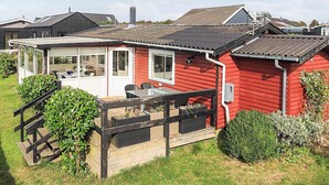 A red wooden house with a glass-enclosed porch and a small deck. - 5 Person Holiday Home in Karrebaeksminde (Karrebæksminde)