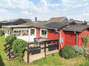 Une maison en bois rouge avec une véranda fermée par des vitres et une petite terrasse.