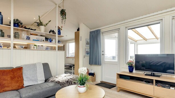 A modern living room with a grey sofa, a round wooden coffee table, a television on a wooden stand, and a large window with curtains. - 5 Person Holiday Home in Karrebaeksminde (Karrebæksminde)