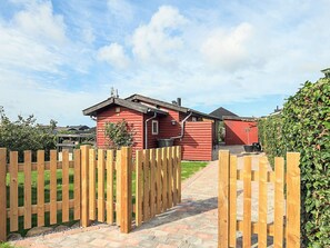 Un bâtiment en bois rouge, avec un chemin pavé de briques menant à une porte en bois.
