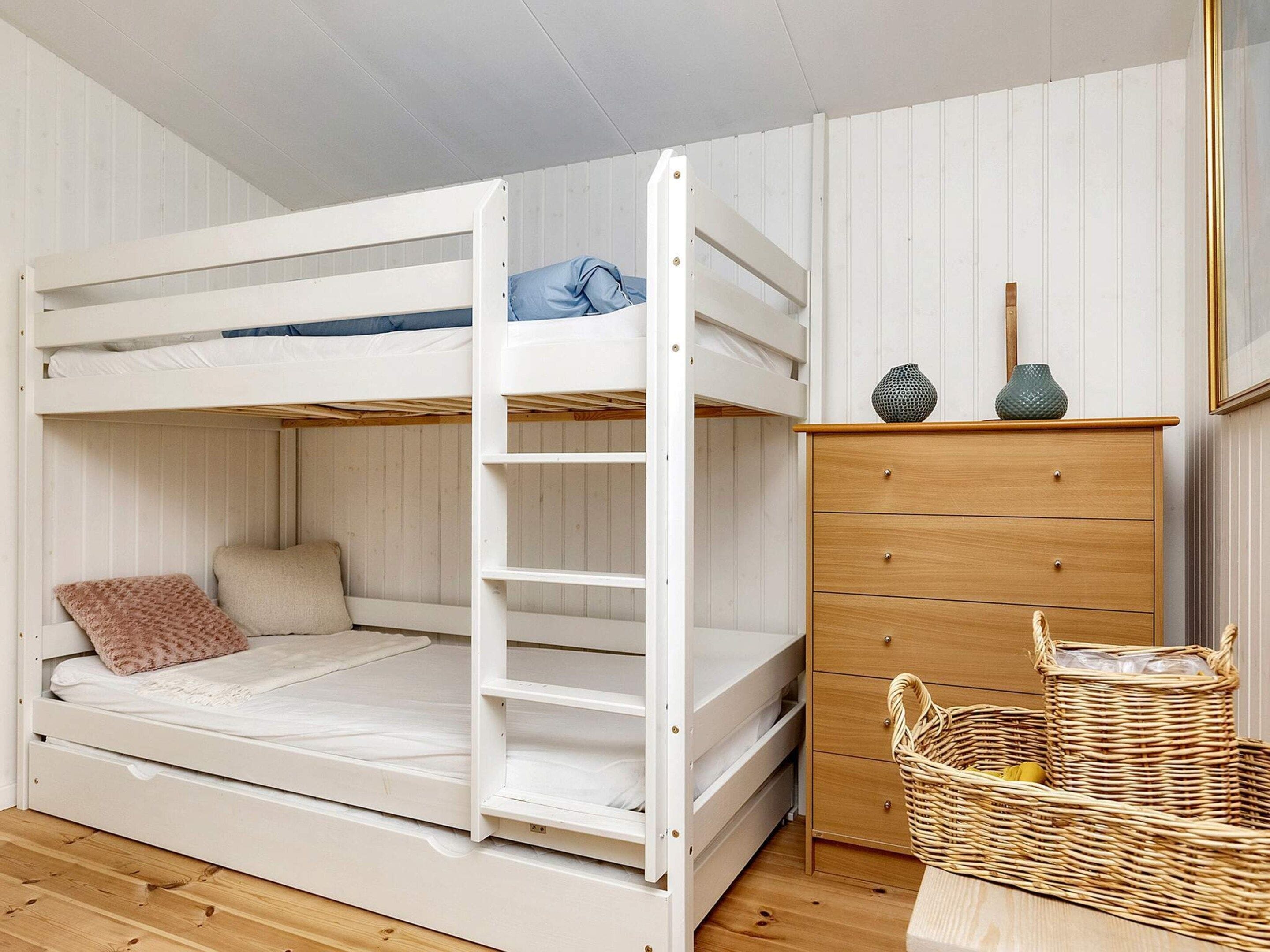 A bunk bed with a ladder, a wooden dresser, and a wicker basket.