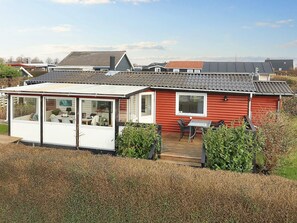 A red mobile home with a covered patio area, a small deck, and a window overlooking a grassy area. - 5 Person Holiday Home in Karrebaeksminde (Karrebæksminde)