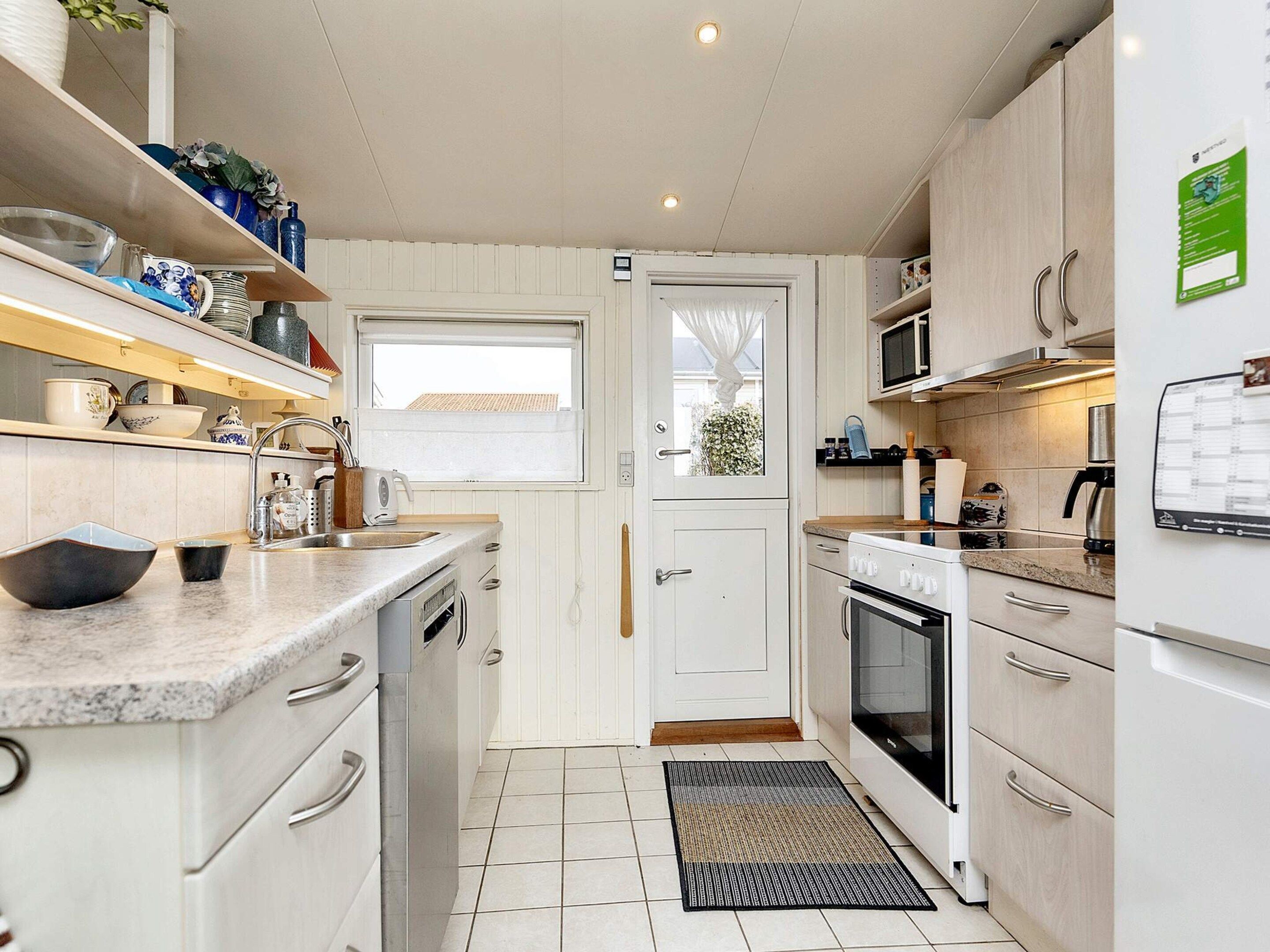 A compact kitchen with white cabinetry, a built-in oven, a microwave, and a sink with a window above it.