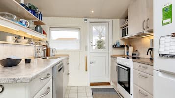 A compact kitchen with white cabinetry, a built-in oven, a microwave, and a sink with a window above it.