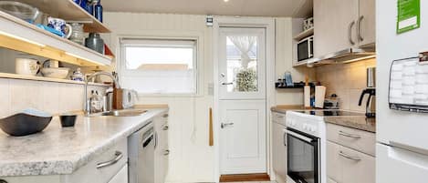 A compact kitchen with white cabinetry, a built-in oven, a microwave, and a sink with a window above it.