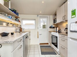 Cocina compacta con armarios blancos, horno empotrado, microondas y pileta con ventana superior.