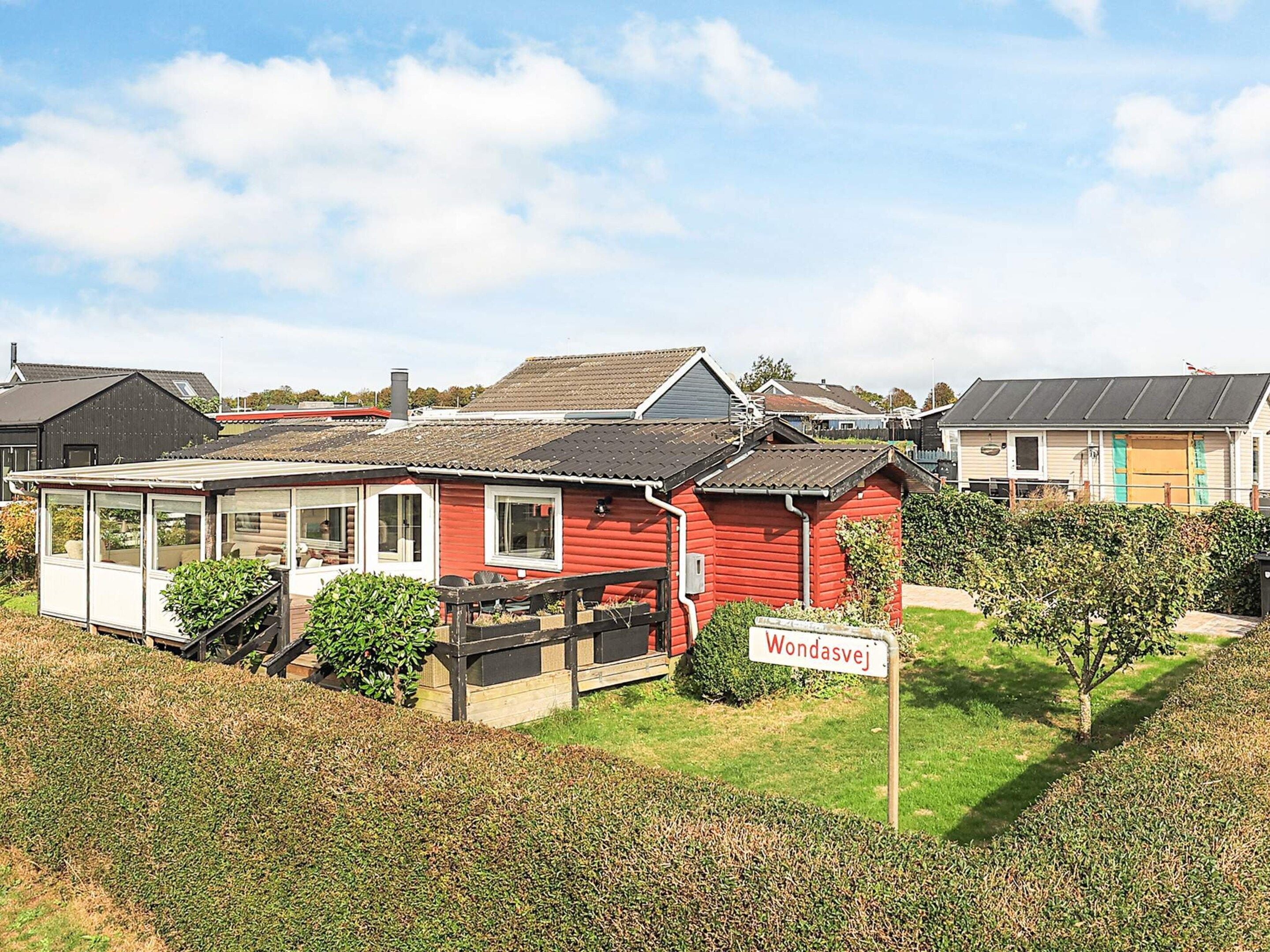 A red wooden house with a sign reading "Wondasvej" in a residential area with other houses.