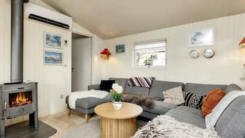 Ein gemütliches Wohnzimmer mit Kaminofen, grauem Sofa, rundem Holztisch und Teppich.