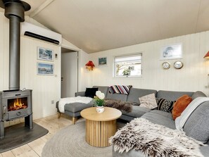 A cozy living room with a wood-burning stove, a grey sofa, a round wooden coffee table, and a rug. - 5 Person Holiday Home in Karrebaeksminde (Karrebæksminde)