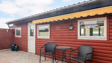 A red wooden building with two windows, a door, and a small outdoor seating area with two chairs and a table.