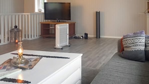 A living room with a white coffee table, a television on a stand, a radiator, and a grey sofa with patterned cushions. - 7 Person Holiday Home in Melfjordbotn-by Traum (Rodoy)