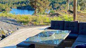 A glass-top table with a bowl, a wicker sofa, and a view of a lake surrounded by trees. - 10 Person Holiday Home in Sondeled-by Traum (Risør)