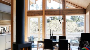 A modern cabin with a large dining area, a wood-burning stove, and large windows offering views of a mountainous landscape. - 10 Person Holiday Home in Sondeled-by Traum (Risør)