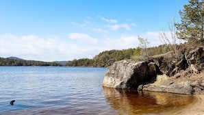 A clear lake with a rocky shoreline and a forested hill in the background. - 10 Person Holiday Home in Sondeled-by Traum (Risør)