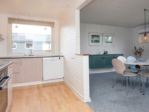 Una cocina moderna con lavavajillas, un comedor con mesa y sillas, y un ventanal con vista a una casa.