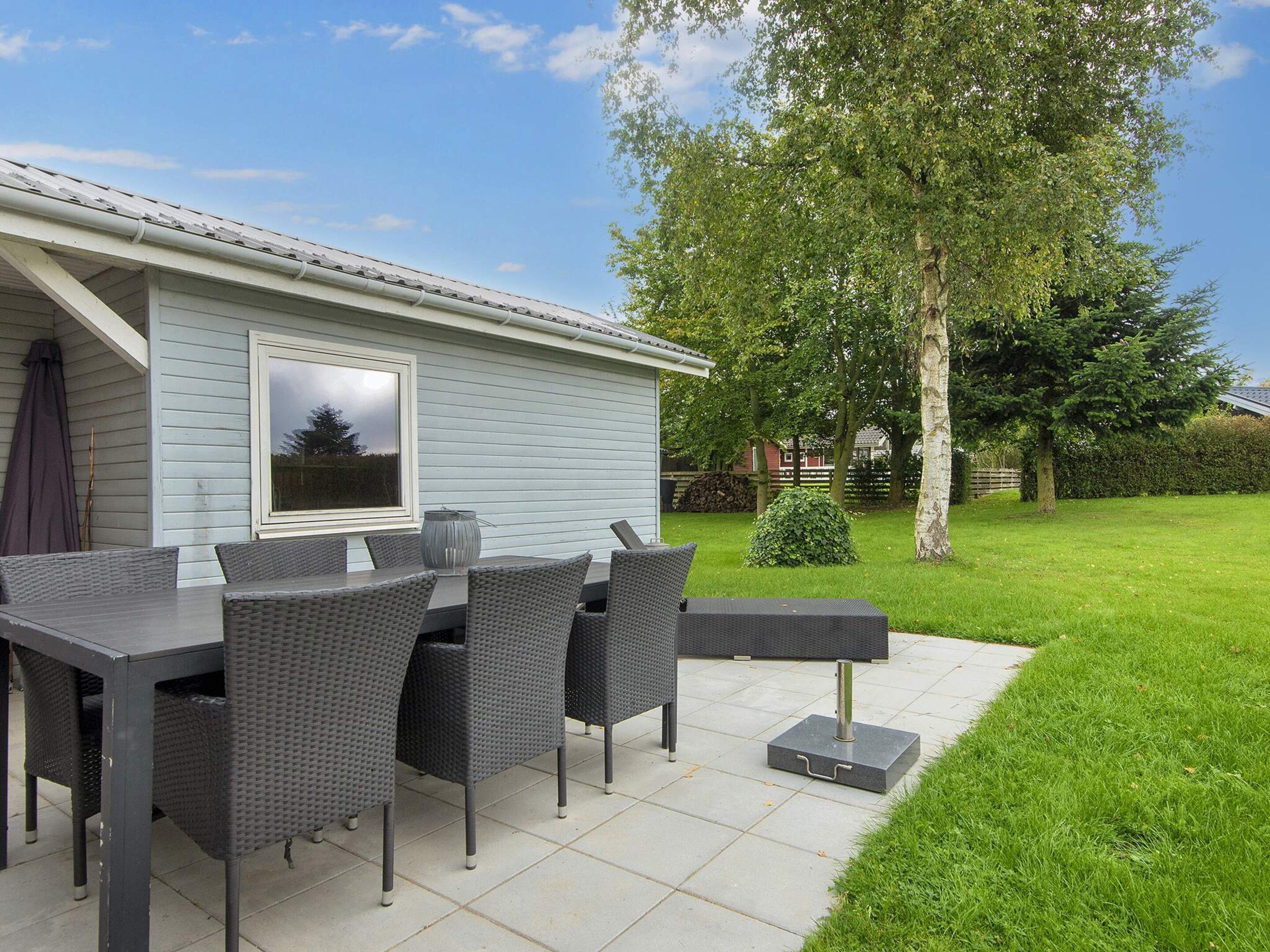 An outdoor patio with a table and chairs, a small potted plant, and a view of a house with a window.