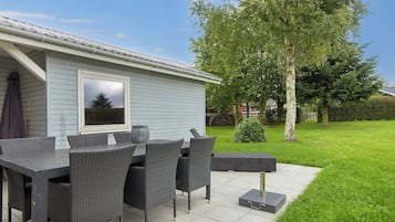 An outdoor patio with a table and chairs, a small potted plant, and a view of a house with a window.