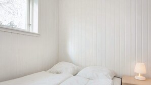 Una cama individual con ropa blanca en una habitación con paneles verticales en las paredes.