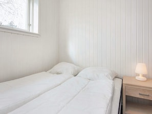 Un lit simple avec une literie blanche, dans une pièce dont les murs sont recouverts de lambris verticaux.