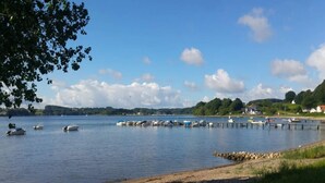 Un lago tranquilo con barcos amarrados en un muelle, rodeado de vegetación y casas.