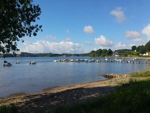 Un lac paisible où des bateaux sont amarrés à un quai, entouré de verdure et de maisons.