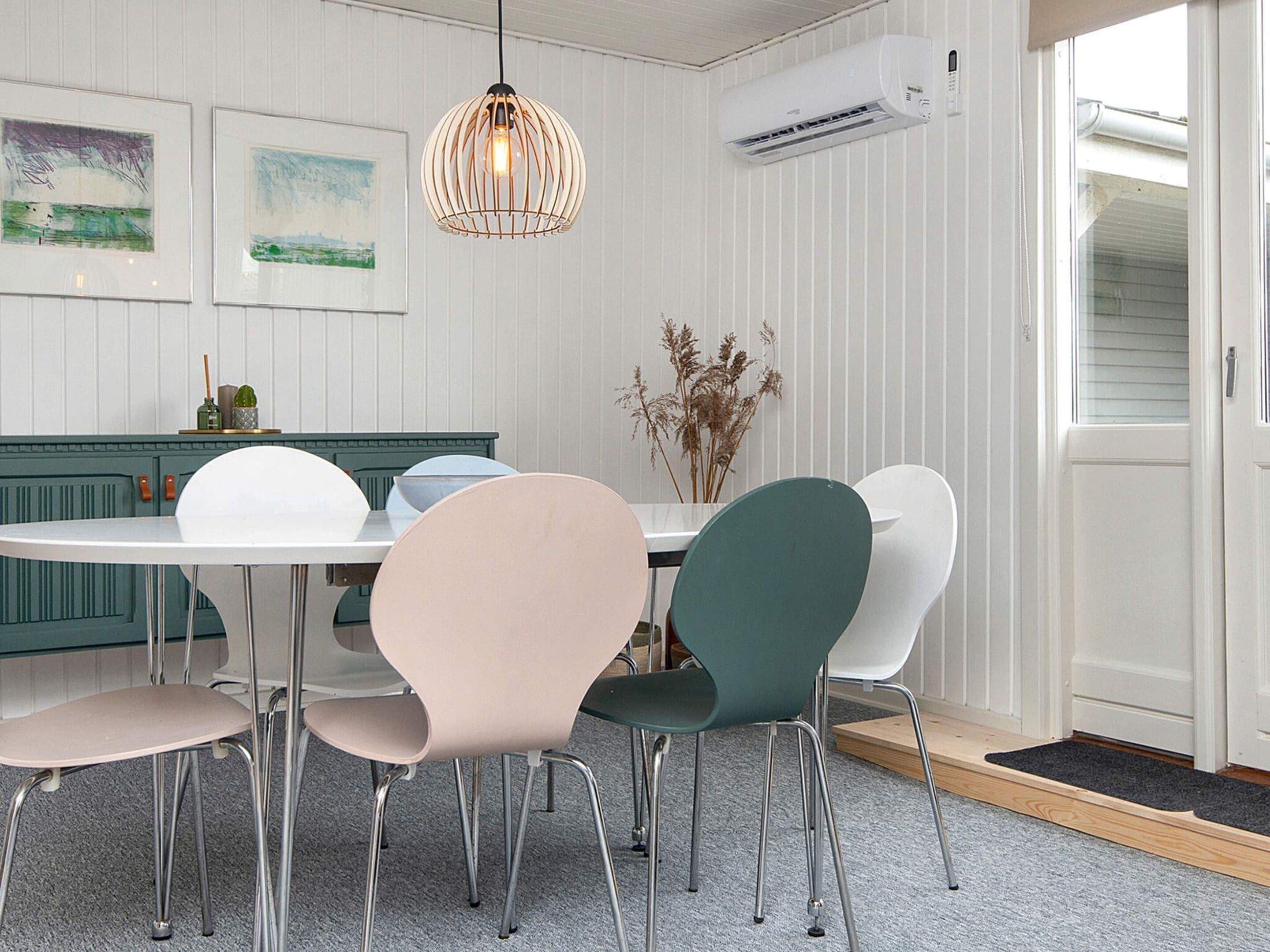 A dining area with a white table, four chairs, a hanging light fixture, and an air conditioning unit.