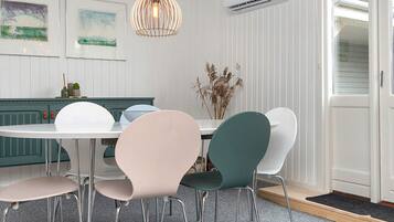 A dining area with a white table, four chairs, a hanging light fixture, and an air conditioning unit.
