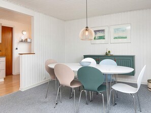 Uma sala de jantar com mesa redonda, cadeiras, luminária pendente e um armário com obras de arte.