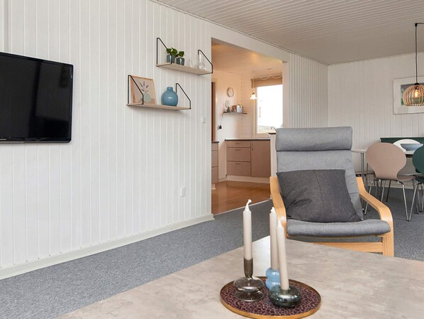 A modern living room with a grey sofa, a flat-screen TV mounted on the wall, and a dining area with a table and chairs. - 6 Person Holiday Home in Haderslev (Haderslev)