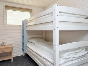 Uma cama de solteiro com estrutura de madeira, uma mesinha de cabeceira com relógio e uma janela com persianas.