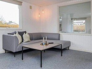Una sala de estar moderna con un sofá seccional gris, una mesita y un amplio ventanal con vistas al exterior.