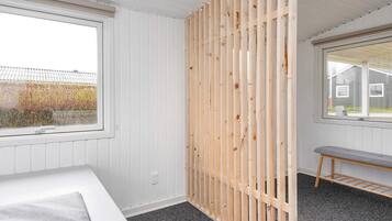 A room with a bed, a window, a wooden partition, and a bench.