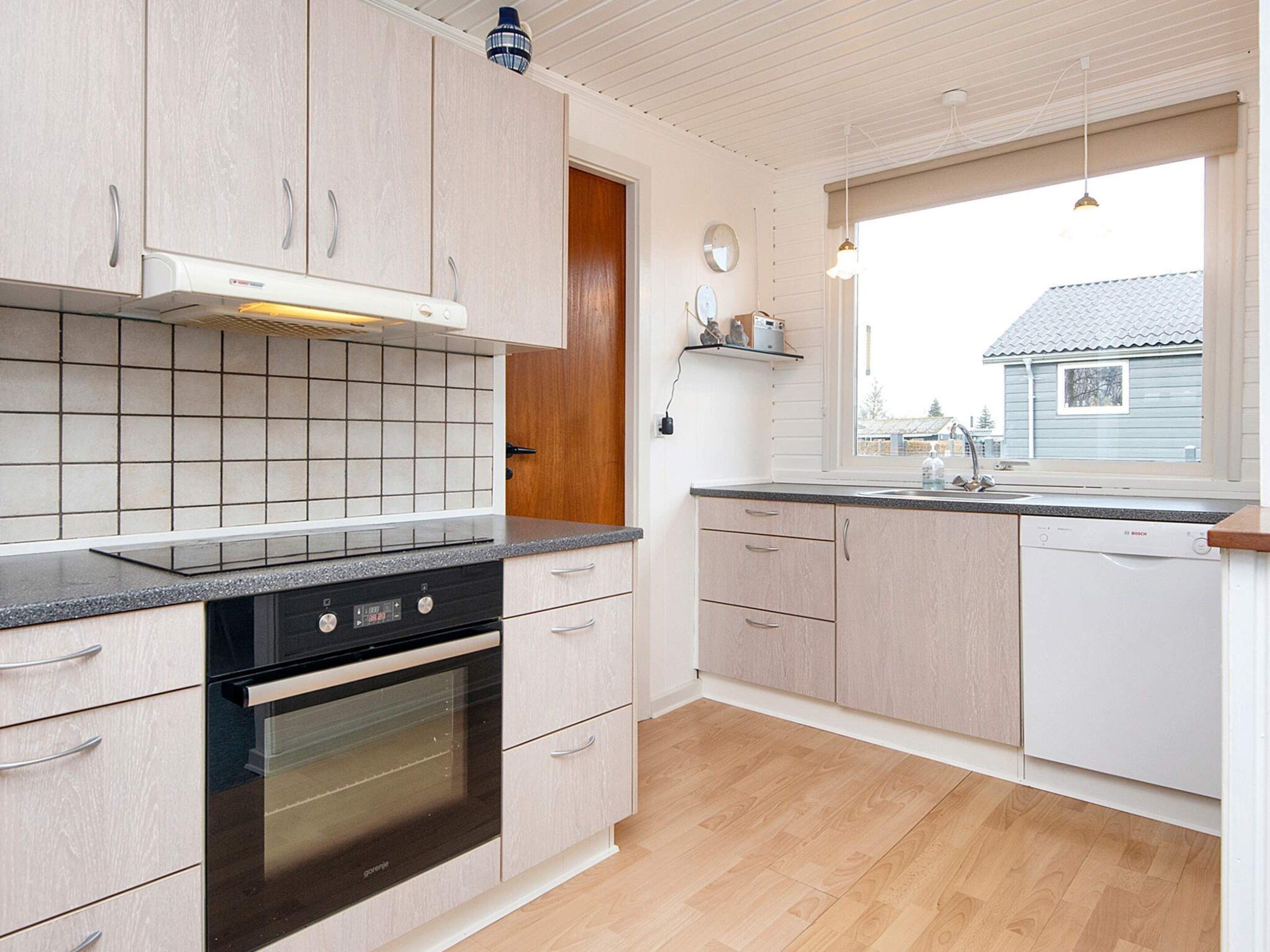 Una cocina moderna con armarios de madera clara, un horno negro y un ventanal con vistas al exterior.