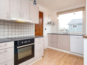 A modern kitchen with light wood cabinets, a black oven, and a window providing a view of the outside. - 6 Person Holiday Home in Haderslev (Haderslev)