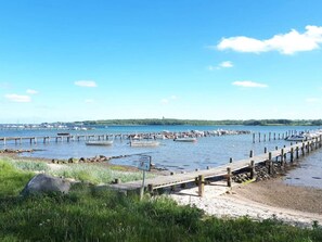 A coastal scene with a wooden pier extending into calm waters, surrounded by greenery and a distant shoreline. - 6 Person Holiday Home in Haderslev (Haderslev)
