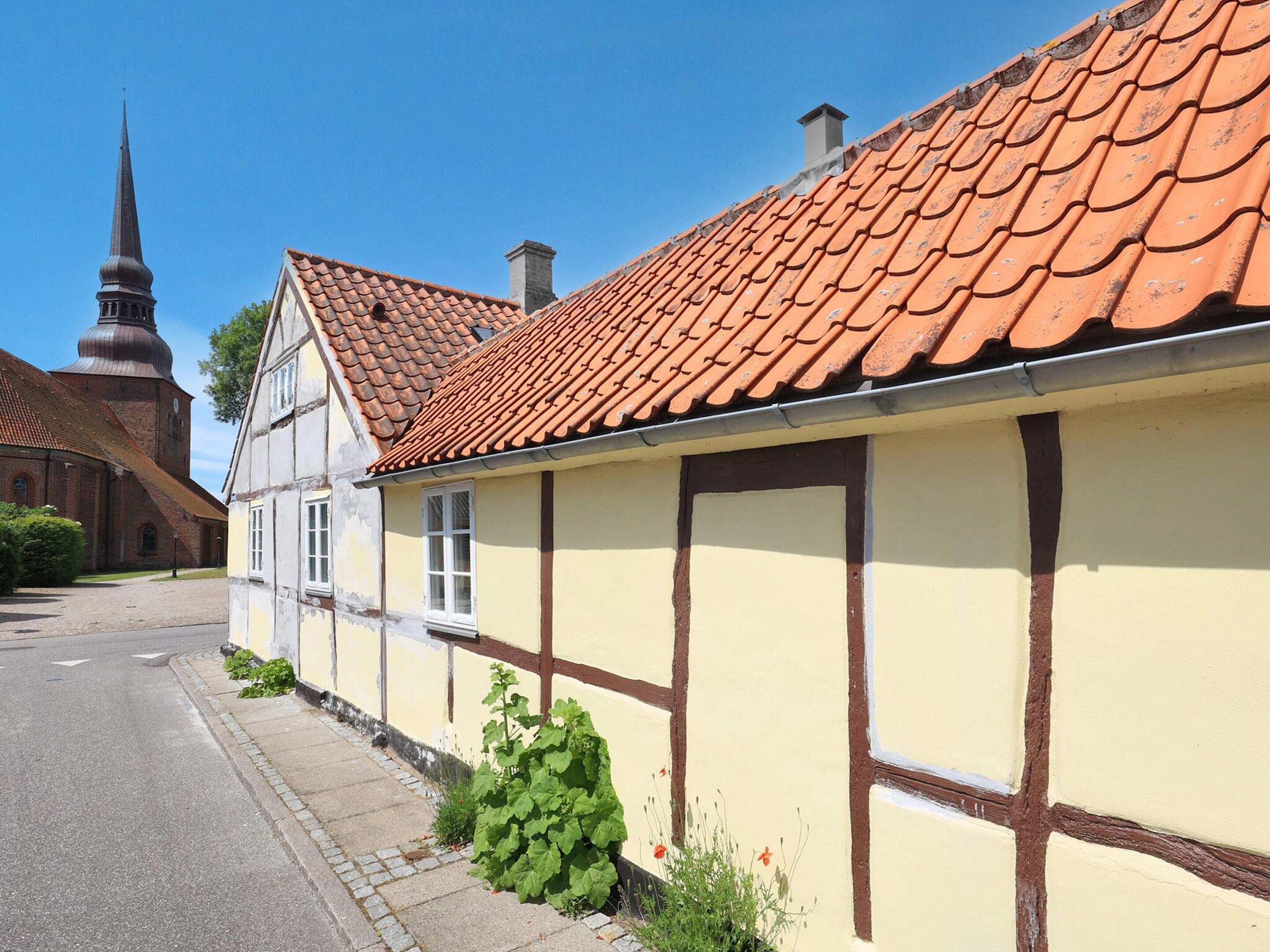 A traditional half-timbered building with a red-tiled roof, adjacent to a church with a pointed steeple.