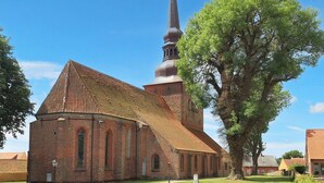 A church with a prominent spire and a large tree in front. - 4 Person Holiday Home in Nysted (Nysted)