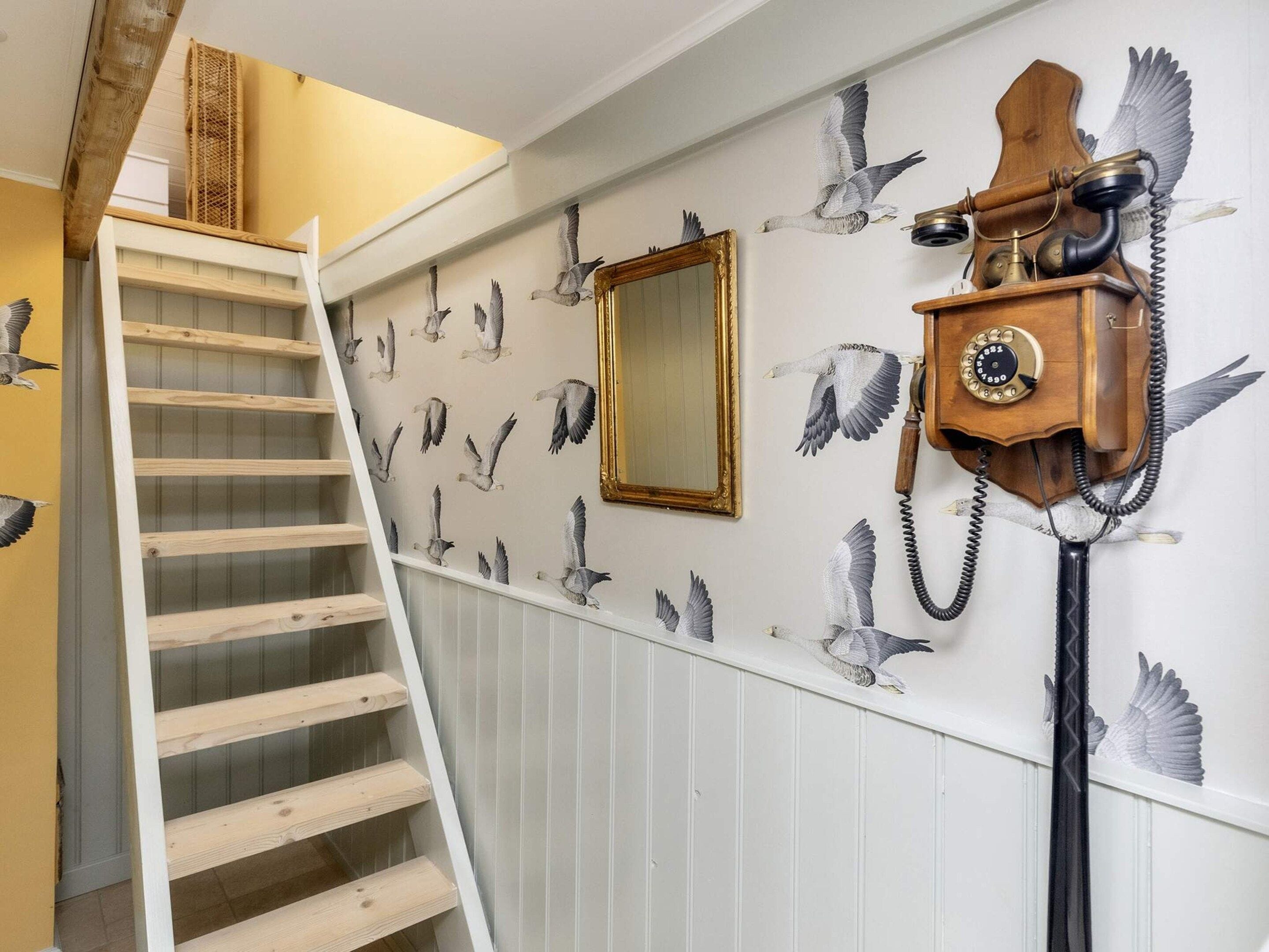 A staircase with a wooden handrail and a wall with a bird mural and a vintage telephone.