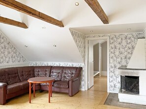 A loft-style living room with exposed wooden beams, a brown leather sectional sofa, a small round table, and a fireplace. - 8 Person Holiday Home in Anneby (Aneby)
